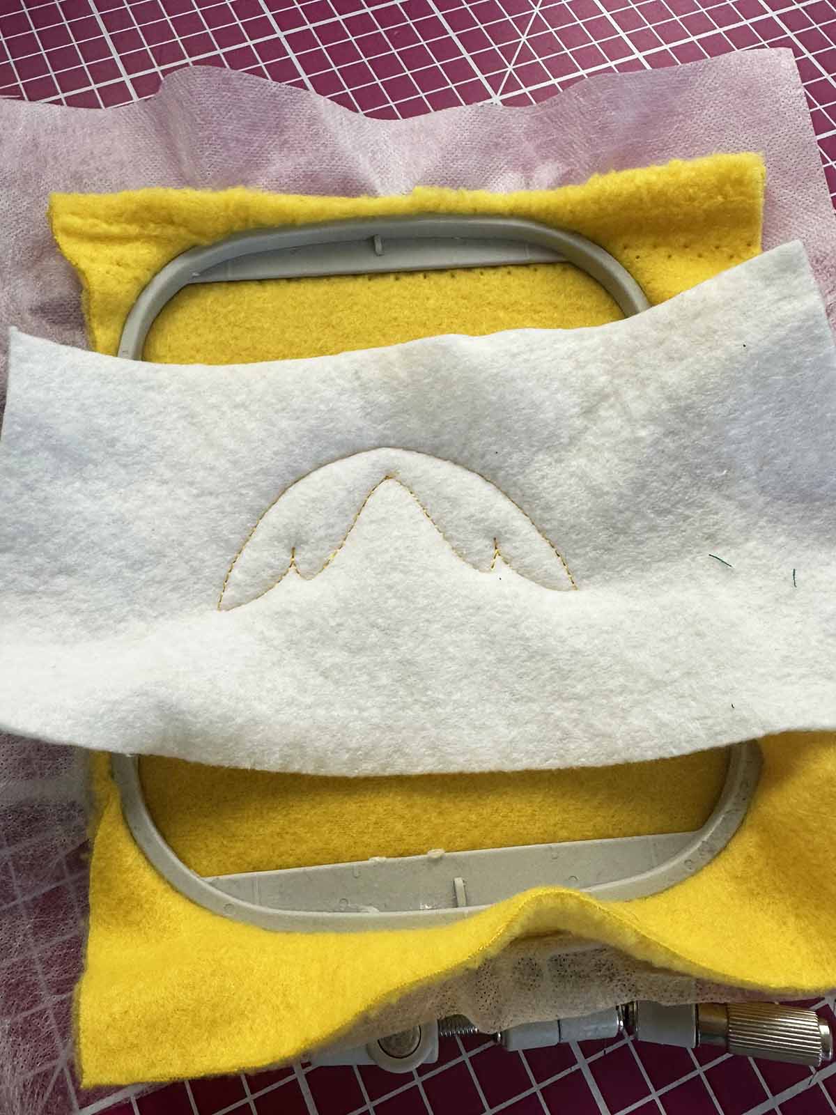 Tear-away stabilizer stitched onto yellow plush fabric in embroidery hoop for ITH plush duck wing preparation