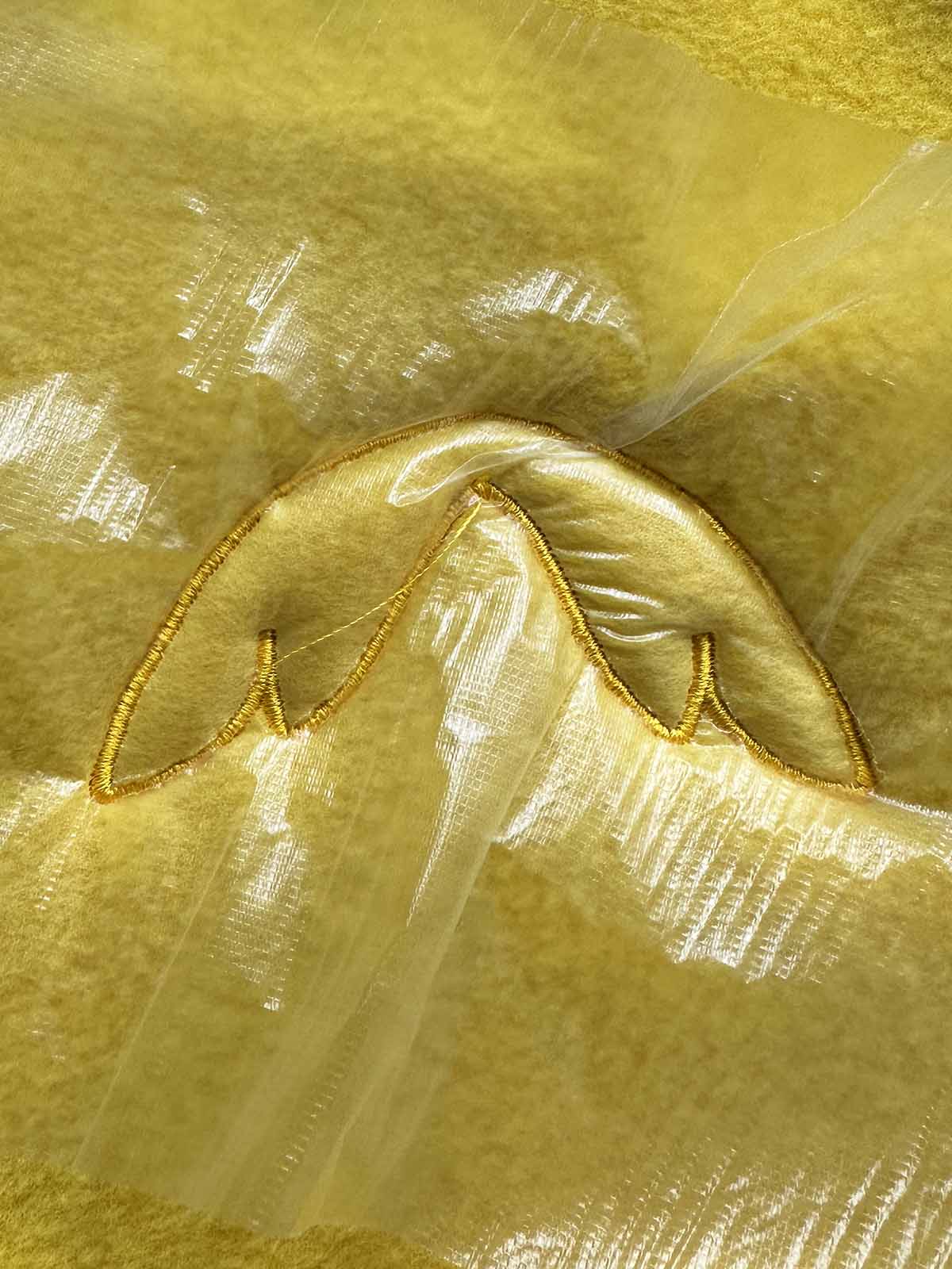 Completed wing embroidery with satin stitch outline on yellow plush fabric inside embroidery hoop