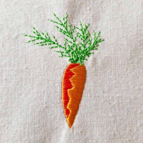 Carrot embroidery design with strong color contrast and green leaves stitched on fabric