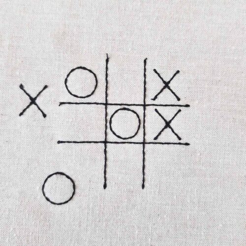 Small tic tac toe embroidery design with grid and X and O symbols stitched on fabric