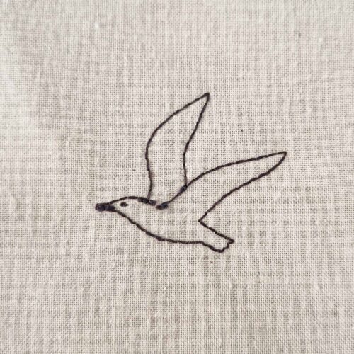Small minimalist dove embroidery design stitched as a simple line art motif on cotton fabric.