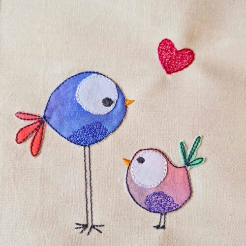 Love birds applique embroidery design stitched on cotton, with a blue bird, a pink bird, and a small red heart.